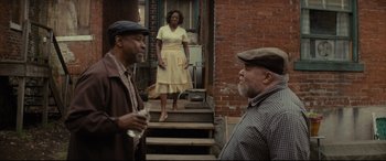 Movie still from “Fences” (2016), directed by Denzel Washington – Two men and a woman standing on steps in front of a brick building; Medium shot, Over the shoulder angle
