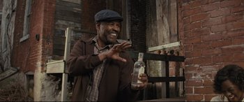 Movie still from “Fences” (2016), directed by Denzel Washington – A man holding a bottle of alcohol and a cell phone in his hand; Medium shot, Low angle