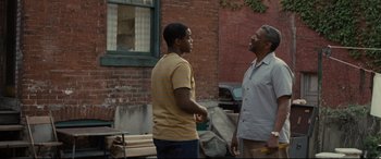 Movie still from “Fences” (2016), directed by Denzel Washington – Two men standing next to each other in front of a brick building; Medium shot, Over the shoulder angle