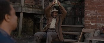 Movie still from “Fences” (2016), directed by Denzel Washington – A man sitting on a bench holding up a cell phone; Medium shot, Low angle