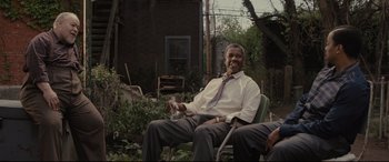 Movie still from “Fences” (2016), directed by Denzel Washington – A man sitting in a chair in a yard; Medium shot, Low angle
