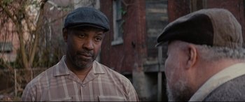 Movie still from “Fences” (2016), directed by Denzel Washington – A man wearing a hat standing next to another man in front of a brick building; Close Up shot, Over the shoulder angle