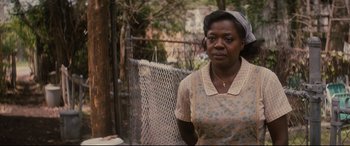 Movie still from “Fences” (2016), directed by Denzel Washington – An older woman standing in front of a chain link fence; Close Up shot, Over the shoulder angle