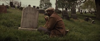 Movie still from “Fences” (2016), directed by Denzel Washington – A man sitting on the ground in front of a grave; Medium shot, High angle