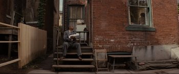 Movie still from “Fences” (2016), directed by Denzel Washington – A man in a suit sitting on a set of stairs; Wide shot, High angle