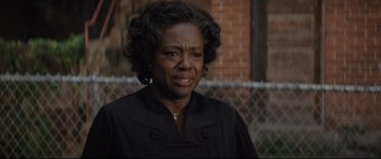 Movie still from “Fences” (2016), directed by Denzel Washington – An older woman in a black dress is standing by a chain link fence; Close Up shot, Over the shoulder angle