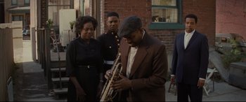 Movie still from “Fences” (2016), directed by Denzel Washington – A man in a brown suit is playing a trumpet; Medium shot, Over the shoulder angle