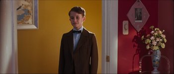 Movie still from “Fido” (2006), directed by Andrew Currie – A boy in a suit and bow tie standing in front of a door; Medium shot, Over the shoulder angle
