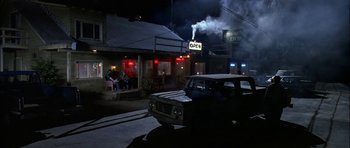 Movie still from “Fire in the Sky” (1993), directed by Robert Lieberman – An old car parked in front of an open sign; Wide shot, High angle