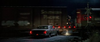Movie still from “Fire in the Sky” (1993), directed by Robert Lieberman – A car driving down a street next to a train; Extreme Wide shot, Low angle
