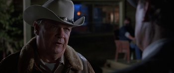 Movie still from “Fire in the Sky” (1993), directed by Robert Lieberman – A man wearing a cowboy hat in a dark room; Close Up shot, Over the shoulder angle