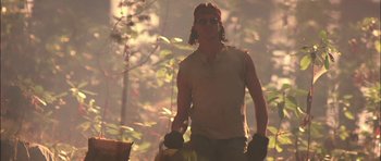 Movie still from “Fire in the Sky” (1993), directed by Robert Lieberman – A man holding a bag while standing next to a tree; Medium shot, Low angle