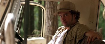 Movie still from “Fire in the Sky” (1993), directed by Robert Lieberman – A man wearing a hat sitting next to a tree; Close Up shot, Low angle