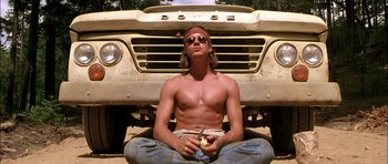 Movie still from “Fire in the Sky” (1993), directed by Robert Lieberman – A man sitting in front of a truck eating a piece of food; Medium shot, Low angle