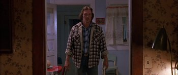 Movie still from “Fire in the Sky” (1993), directed by Robert Lieberman – A man standing in a room wearing a plaid shirt; Medium shot, Low angle
