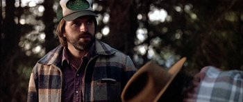 A man wearing a hat standing next to a tree