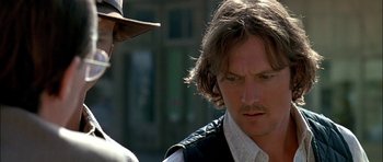 Movie still from “Fire in the Sky” (1993), directed by Robert Lieberman – A man with long brown hair wearing a hat; Close Up shot, Over the shoulder angle