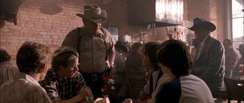 Movie still from “Fire in the Sky” (1993), directed by Robert Lieberman – A man standing next to a group of people in front of a brick wall; Medium shot, Over the shoulder angle