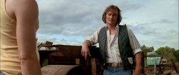 Movie still from “Fire in the Sky” (1993), directed by Robert Lieberman – A man leaning on a fence in a rural area; Medium shot, Low angle