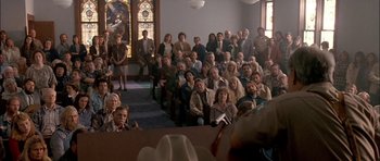 Movie still from “Fire in the Sky” (1993), directed by Robert Lieberman – A group of people sitting in front of a crowd; Wide shot, High angle