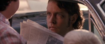 Movie still from “Fire in the Sky” (1993), directed by Robert Lieberman – A person sitting in a car reading a newspaper; Close Up shot, Over the shoulder angle