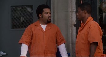 Movie still from “First Sunday” (2008), directed by David E. Talbert – Two men in orange jumpsuits standing next to each other; Medium shot, Over the shoulder angle