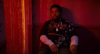 Movie still from “First Sunday” (2008), directed by David E. Talbert – A man sitting on a chair in a room with red walls; Medium shot, High angle