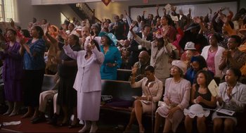Movie still from “First Sunday” (2008), directed by David E. Talbert – A group of people sitting and standing in a room; Wide shot, High angle