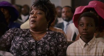 Movie still from “First Sunday” (2008), directed by David E. Talbert – A woman in a crowd of people sitting in a room; Close Up shot, Low angle