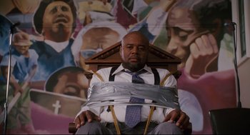 Movie still from “First Sunday” (2008), directed by David E. Talbert – A man tied up in a chair with duct tape around his neck; Medium shot, Low angle