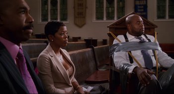 Movie still from “First Sunday” (2008), directed by David E. Talbert – A woman sitting in front of a man in front of a podium; Medium shot, Low angle