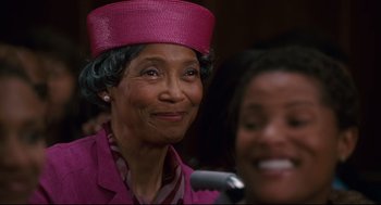 Movie still from “First Sunday” (2008), directed by David E. Talbert – An older woman wearing a pink hat and smiling; Close Up shot, Over the shoulder angle