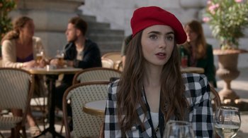 Movie still from “Emily in Paris” (2020), created by Darren Star – A woman in a red hat sitting at a table; Medium shot, Over the shoulder angle