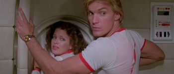 Movie still from “Flash Gordon” (1980), directed by Mike Hodges – A man and a woman in white shirts and red trim; Medium shot, Low angle