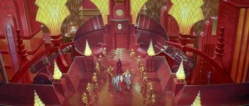 Movie still from “Flash Gordon” (1980), directed by Mike Hodges – A group of people standing in a room with gold statues; Extreme Wide shot, High angle