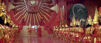 Movie still from “Flash Gordon” (1980), directed by Mike Hodges – A group of people standing in a room with red walls; Extreme Wide shot, High angle
