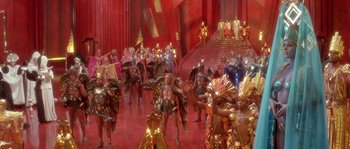 Movie still from “Flash Gordon” (1980), directed by Mike Hodges – A group of people dressed in gold and red costumes; Extreme Wide shot, High angle