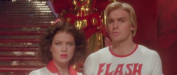 Movie still from “Flash Gordon” (1980), directed by Mike Hodges – A man and a woman standing next to each other in front of a statue; Close Up shot, Low angle
