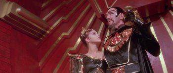 Movie still from “Flash Gordon” (1980), directed by Mike Hodges – A man and a woman standing next to each other in front of a red wall; Medium shot, Low angle
