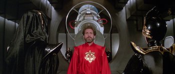Movie still from “Flash Gordon” (1980), directed by Mike Hodges – A man in a red robe standing in front of a machine; Medium shot, Low angle