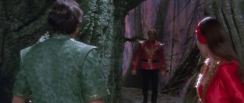 Movie still from “Flash Gordon” (1980), directed by Mike Hodges – A man in a red jacket standing in front of a forest; Wide shot, Over the shoulder angle