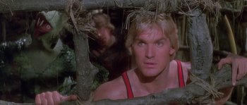 Movie still from “Flash Gordon” (1980), directed by Mike Hodges – A man with blonde hair and a red tank top looking through a tree branch; Close Up shot, Low angle