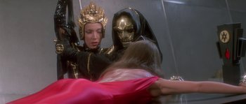 Movie still from “Flash Gordon” (1980), directed by Mike Hodges – Two people dressed in black and gold are fighting; Medium shot, Over the shoulder angle