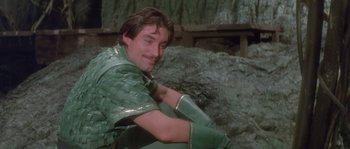 Movie still from “Flash Gordon” (1980), directed by Mike Hodges – A man sitting on the ground wearing a green outfit; Medium shot, Over the shoulder angle