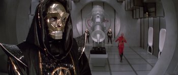 Movie still from “Flash Gordon” (1980), directed by Mike Hodges – A group of people in costumes in a room; Medium shot, Low angle