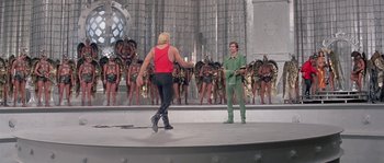 Movie still from “Flash Gordon” (1980), directed by Mike Hodges – A man and a woman are standing in front of a group of people; Wide shot, Over the shoulder angle