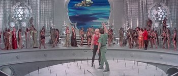 Movie still from “Flash Gordon” (1980), directed by Mike Hodges – A group of people standing in front of an audience; Wide shot, High angle