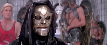 Movie still from “Flash Gordon” (1980), directed by Mike Hodges – A person wearing a gold mask and a black robe; Close Up shot, Low angle