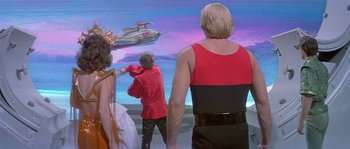 Movie still from “Flash Gordon” (1980), directed by Mike Hodges – A group of people standing in front of a screen; Wide shot, Over the shoulder angle
