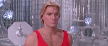 Movie still from “Flash Gordon” (1980), directed by Mike Hodges – A man with blonde hair wearing a red tank top; Close Up shot, Low angle